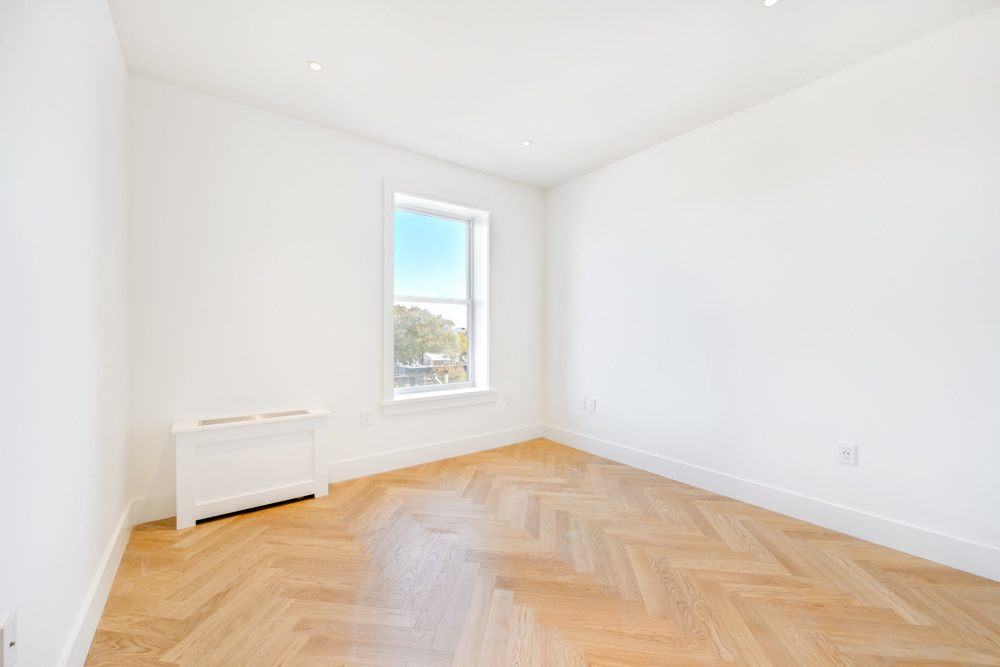 a living room with white walls and wooden floors and a window